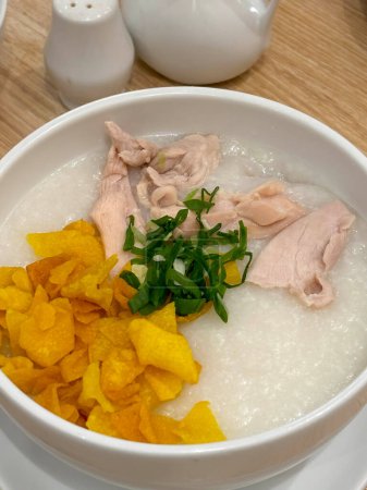 Reisbrei mit geschreddertem Huhn Bubur Ayam genannt, serviert mit Crackern und in Scheiben geschnittenen Frühlingszwiebeln und anderen Gewürzen im Restaurant