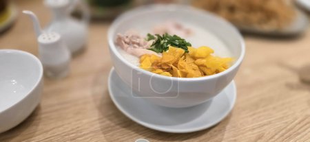 bouillie de riz avec poulet râpé appelé bubur ayam servi avec des craquelins et des tranches d'oignon de printemps et d'autres condiments dans le restaurant