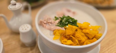 rice porridge with shredded chicken called bubur ayam served with crackers and sliced spring onion and others condiments in restaurant