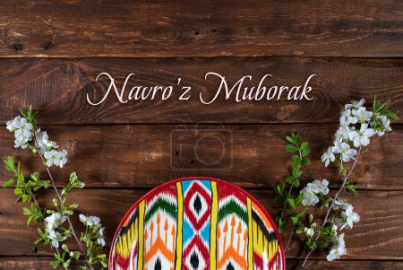 Rishtan Uzbek national plate and  blooming cherry flowers on wooden background. Postcard for Navruz holiday with text
