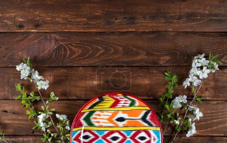 Rishtan Uzbek national plate and  blooming cherry flowers on wooden background. Space for text. Horizontal adras pattern