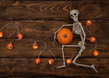 Téléchargez les photos : Squelette avec citrouille sur fond bois avec petite guirlande de citrouille. Concept Halloween - en image libre de droit