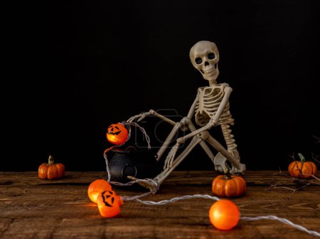 Téléchargez les photos : Squelette avec citrouilles et chaudron de sorcière fond en bois avec petite guirlande de citrouille. Concept Halloween - en image libre de droit