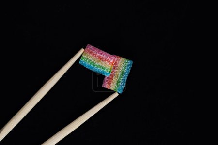 Photo for Chopsticks holding rainbow marmalade isolated on black background - Royalty Free Image
