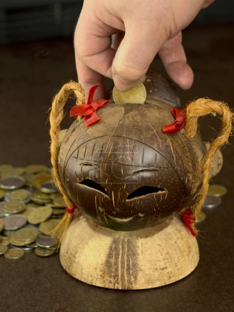 Ein ungewöhnliches Sparschwein für Geld aus Kokosfrüchten. Ein Sparschwein mit kleinem Metallgeld beladen