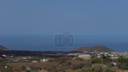 A scenic view of a coastal town and the ocean, with a cold lava flow on the mountainside.