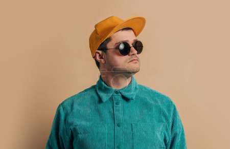 Téléchargez les photos : Stylish caucasian man in green shirt, sunglasses and cap on brown background - en image libre de droit