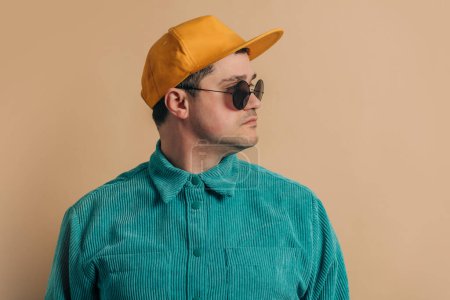 Téléchargez les photos : Stylish caucasian man in green shirt, sunglasses and cap on brown background - en image libre de droit