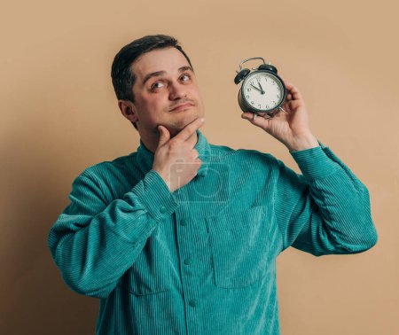 Foto de Elegante hombre caucásico en camisa verde con reloj despertador vintage sobre fondo marrón - Imagen libre de derechos