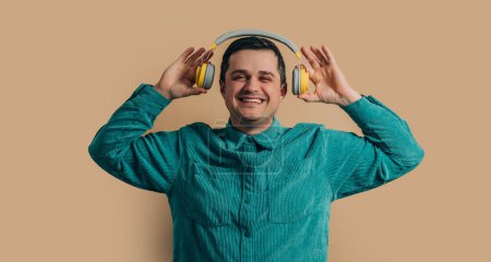 Photo pour Smiling caucasian man in green shirt with headphones on brown background - image libre de droit