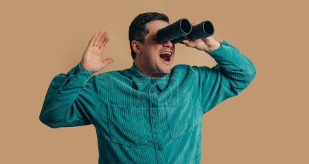 Téléchargez les photos : Stylish caucasian man in green shirt with binoculars on brown background - en image libre de droit