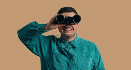 Téléchargez les photos : Stylish caucasian man in green shirt with binoculars on brown background - en image libre de droit