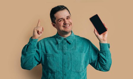 Téléchargez les photos : Stylish caucasian man in green shirt with smartphone on brown background - en image libre de droit