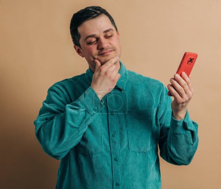 Téléchargez les photos : Stylish caucasian man in green shirt with smartphone on brown background - en image libre de droit