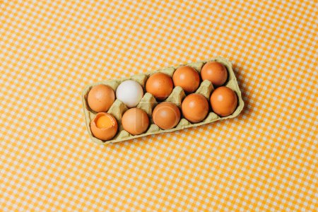 Photo for Ten chicken eggs in carton egg box on plaid tablecloth, top view - Royalty Free Image