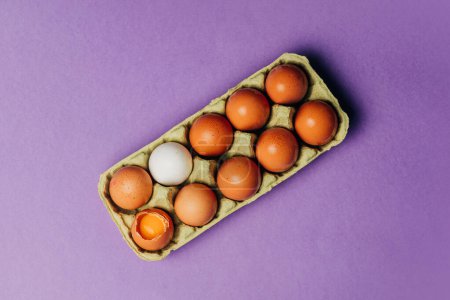 Foto de Diez huevos de pollo en caja de cartón sobre fondo púrpura, vista superior - Imagen libre de derechos