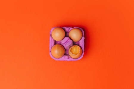 Photo for Four chicken eggs in purple egg box on orange background, Top view - Royalty Free Image