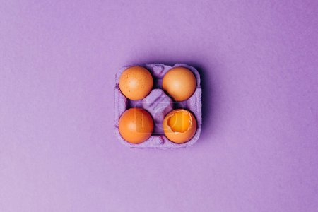 Foto de Cuatro huevos de pollo en caja de huevo púrpura sobre fondo púrpura, vista superior - Imagen libre de derechos