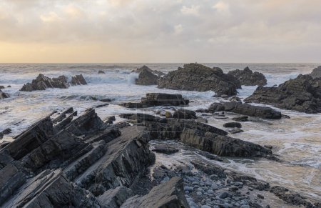 Foto de Mirando hacia fuera en afloramientos rocosos en un mar áspero del invierno con el sol que comienza a bajar - Imagen libre de derechos