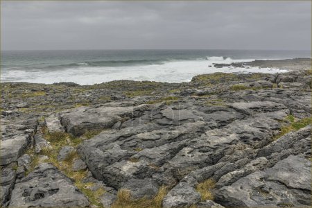 Limestone pavement leading down to a stormy sea with lichen and sea grass growing inbetween the cracks
