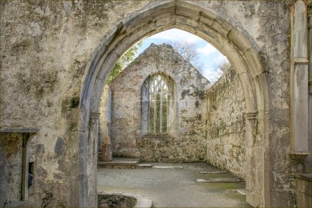 Looking through the archway of a derelict abbey made of light coloured stone  at a gable end