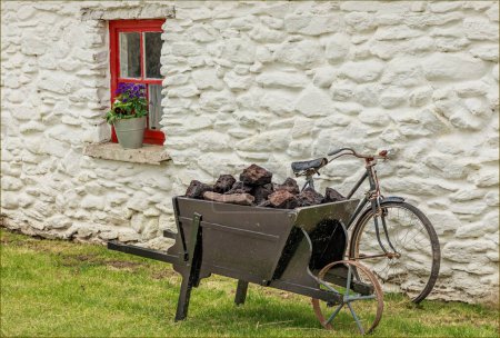 Wooden wheel barrow of peat outside a traditional iwhite painted rish cottage