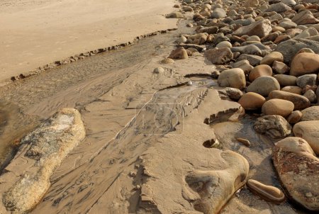 Eau coulant entre de grandes pierres et des rochers sur une plage créant une rivière à la mer