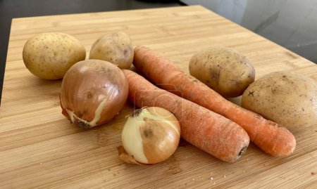Photo for Vegetables potatoes, carrots and onions lie on a wooden board in the kitchen. High quality photo - Royalty Free Image