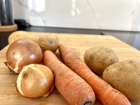 Photo for Vegetables potatoes, carrots and onions lie on a wooden board in the kitchen. High quality photo - Royalty Free Image