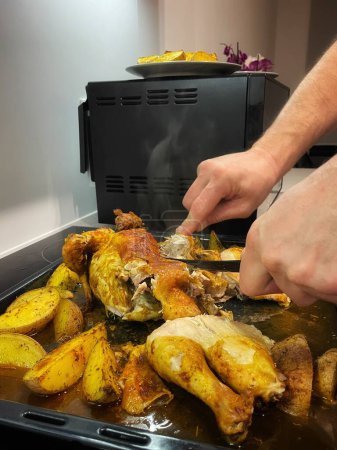 Les mains coupent le poulet cuit au four avec des pommes de terre au couteau. Photo de haute qualité