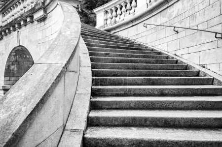 Photo for An elegant old stone staircase with a railing curves up. Black and white photo - Royalty Free Image