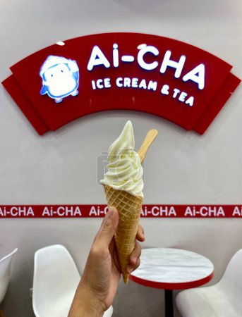 Téléchargez les photos : Pekalongan, Indonésie, 30 août 2023 : tenant un cône de crème glacée avec le logo Ai-CHA en arrière-plan. Photo de crème glacée dans les mains d'un Asiatique. Glace parfumée à la vanille. - en image libre de droit
