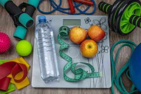 Fitness equipment. Female gym accessories, yoga items, various sports equipment, smart scales, water bottle, dumbbells, skipping rope, fitness rubber bands, balls, apples, measuring tape. Health set.