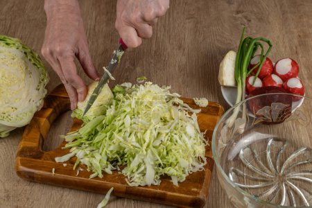 Photo for Housewife cuts white cabbage thinly for making a vegetable salad. Close-up of female hands chopping white cabbage on a wooden cutting board on the kitchen table. The concept of veganism and raw food. - Royalty Free Image