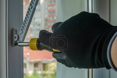 Photo for The worker with a screwdriver screws the fixing screw into the window frame, setting the window opening regulator. Installation of a limiter on a plastic window frame. Window guard fixture. - Royalty Free Image