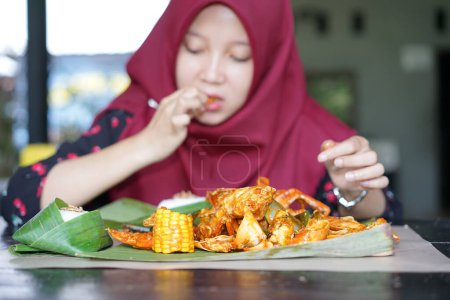 Foto de Una mujer en un hiyab está comiendo mariscos de cangrejo - Imagen libre de derechos