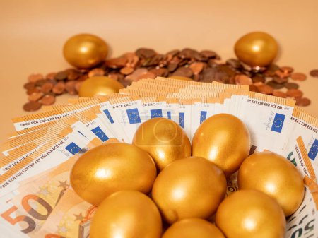 Golden eggs on money. Golden chicken eggs on euro banknotes and coins. Wealth symbol. Savings and investment. Poster 632092686