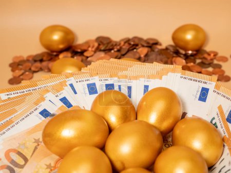 Golden eggs on money. Golden chicken eggs on euro banknotes and coins. Wealth symbol. Savings and investment. Poster 632092698