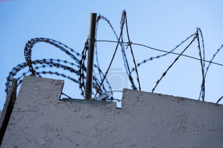 Foto de Alambre de púas en la parte superior de una cerca contra un cielo azul. Concepto de libertad. - Imagen libre de derechos