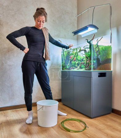 A woman stands near the white bucket in front of the aquarium aquascape. Water changing concept