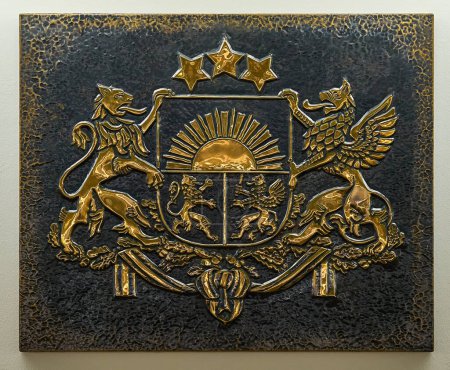 Foto de Primer plano del escudo de armas de color oro de Letonia grabado en relieve sobre una placa de metal oscuro en relieve. - Imagen libre de derechos