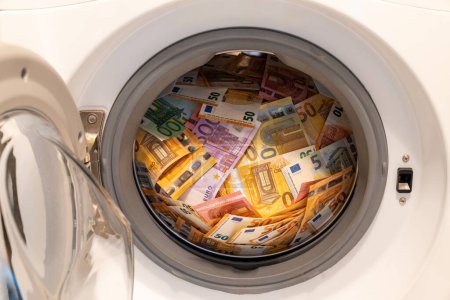 Téléchargez les photos : Gros plan d'une grosse pile d'argent dans une machine à laver ouverte. Concept de blanchiment d'argent. - en image libre de droit