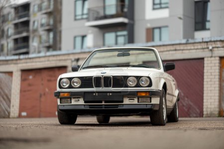 Photo for Riga, Latvia - April 1, 2024: The white classic convertible BMW E30 car with opened roof. An old garages and modern building on the background. - Royalty Free Image