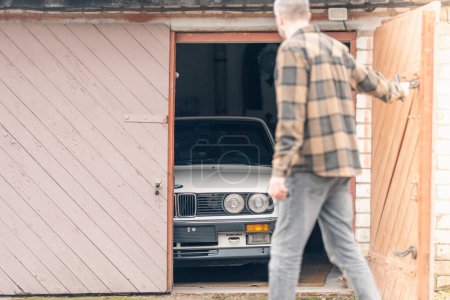 Photo for Riga, Latvia - April 1, 2024: A car owner looking on his white classic convertible BMW E30 car in the half opened garage. - Royalty Free Image