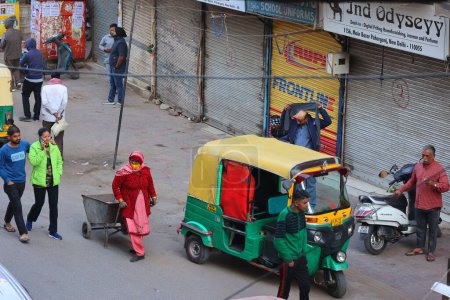 Téléchargez les photos : DELHI INDIA - 02 11 2023 : Femme Rajasthan traditionnelle portant un sari rose, au travail, portant des ustensiles de nettoyage dans un camion à main en acier avec un balai - en image libre de droit