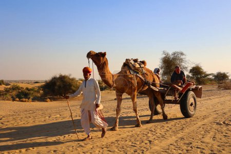 Foto de DESERT THAR RAJASTHAN INDIA - 02 13 2023: Camaleero indio (conductor de camellos) con camellos en dunas del desierto de Thar. Jaisalmer, Rajastán, India - Imagen libre de derechos