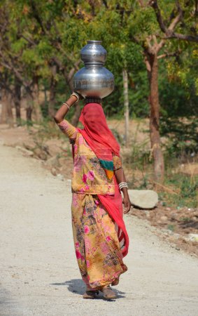Foto de RURAL RAJASTHAN INDIA - 02 13 2023: Vida tribal pueblo vida mujeres llevando agua en macetas en cabeza escasez de agua de verano - Imagen libre de derechos