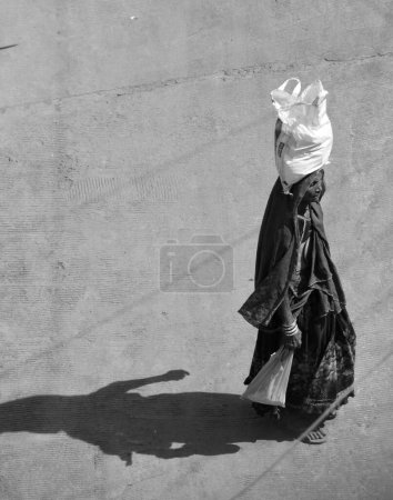 Foto de RURAL RAJASTHAN INDIA - 02 15 2023: Mujer del pueblo llevando sus cosas en la cabeza y volviendo a casa - Imagen libre de derechos