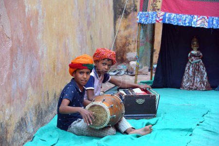 Foto de JAIPUR RAJASTHAN INDIA - 04 01 2023: Rajasthani niños artista de la música en traje tradicional, jugando tamtam en la salida del palacio de la ciudad - Imagen libre de derechos