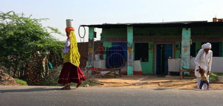 Téléchargez les photos : RURAL RAJASTHAN INDIA - 03 01 2023 : Rajasthani portant des pots d'eau dans la tête. Le pays compte 18 % de la population mondiale, mais seulement 4 % de ses ressources en eau - en image libre de droit